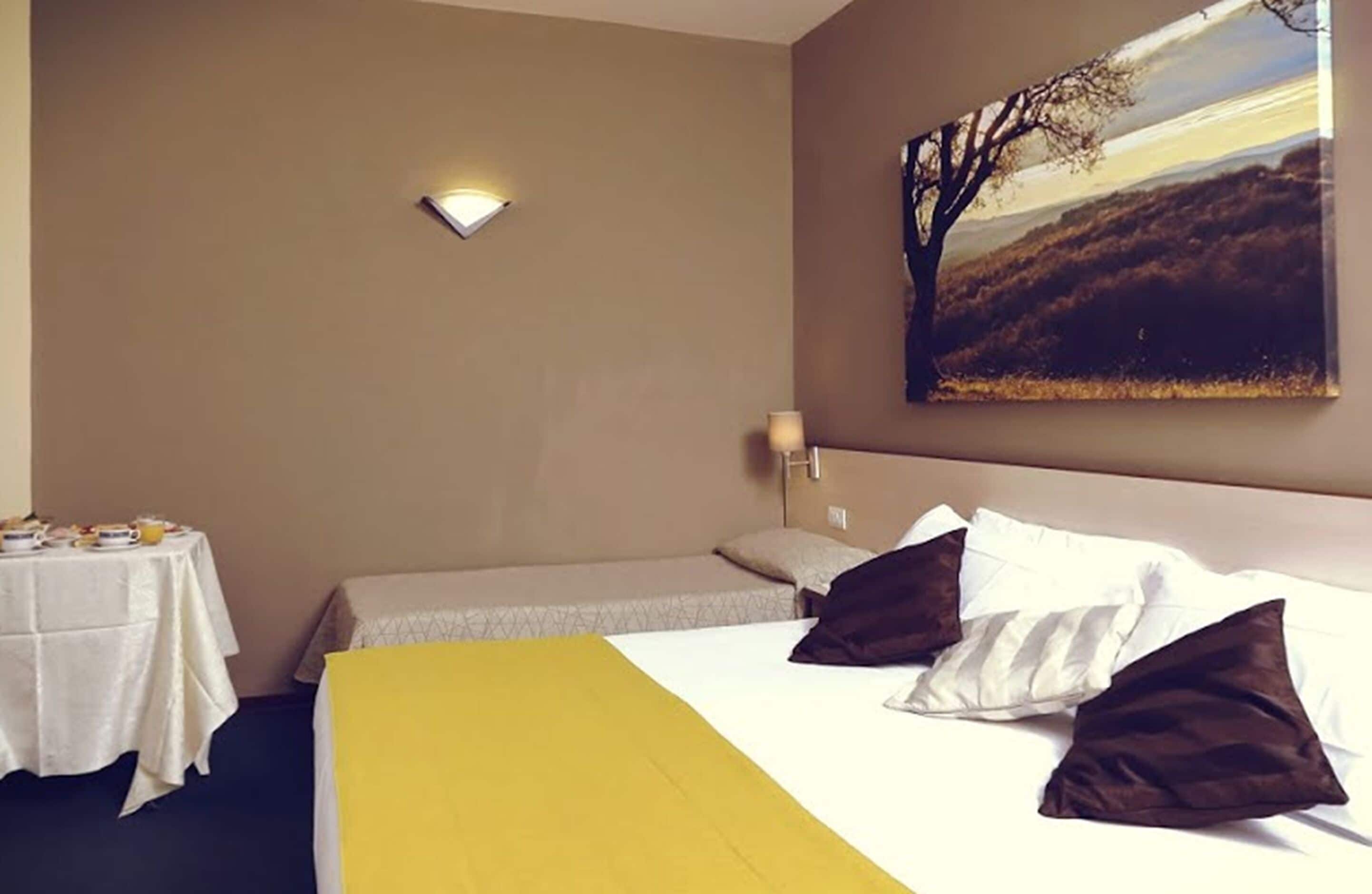 Ein Hotelzimmer mit Bett, Nachttisch mit Lampe, einem Bild an der Wand und einer gelben Bettdecke.