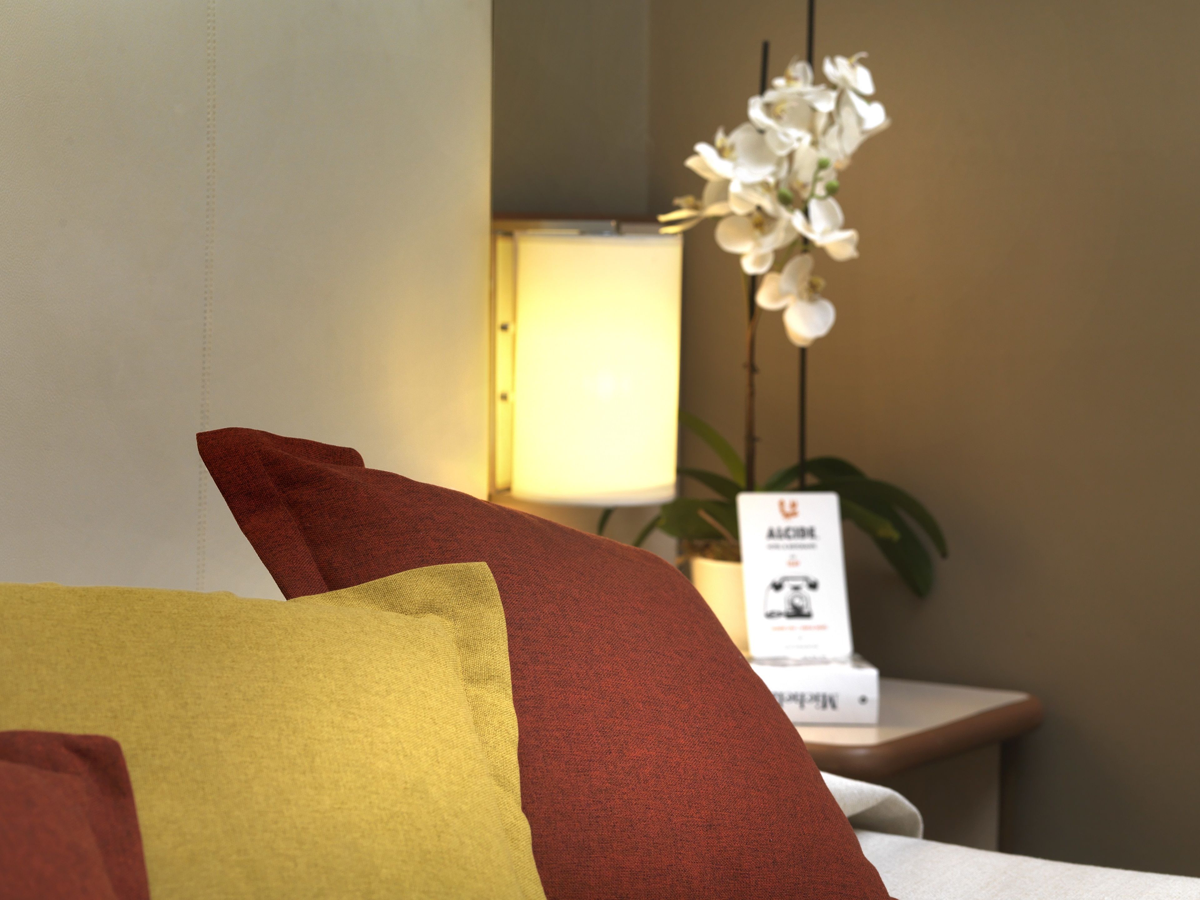 A hotel room with a bed, pillows, a nightstand with a lamp, and a sign.