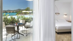 Habitación de hotel con cama, una pequeña mesa con sillas y vistas a una piscina y montañas.