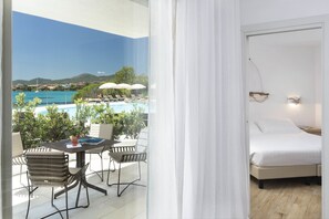 A hotel room with a bed, a small table with chairs, and a view of a pool and mountains.