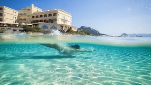 On voit clairement une piscine avec une personne qui plonge, des bâtiments en arrière-plan et une montagne.