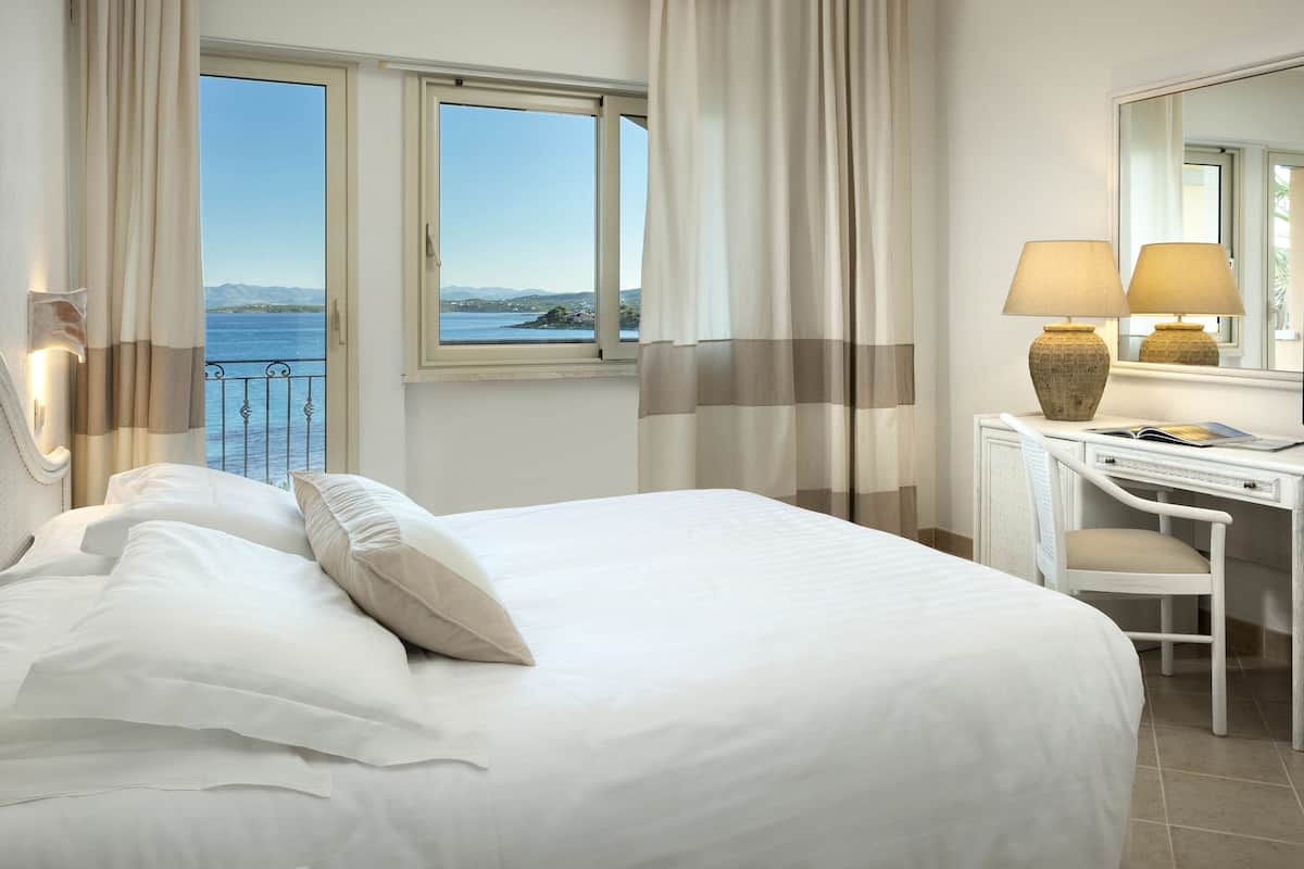 Ein Hotelzimmer mit Bett, Schreibtisch, Stuhl, Lampe und Meerblick.