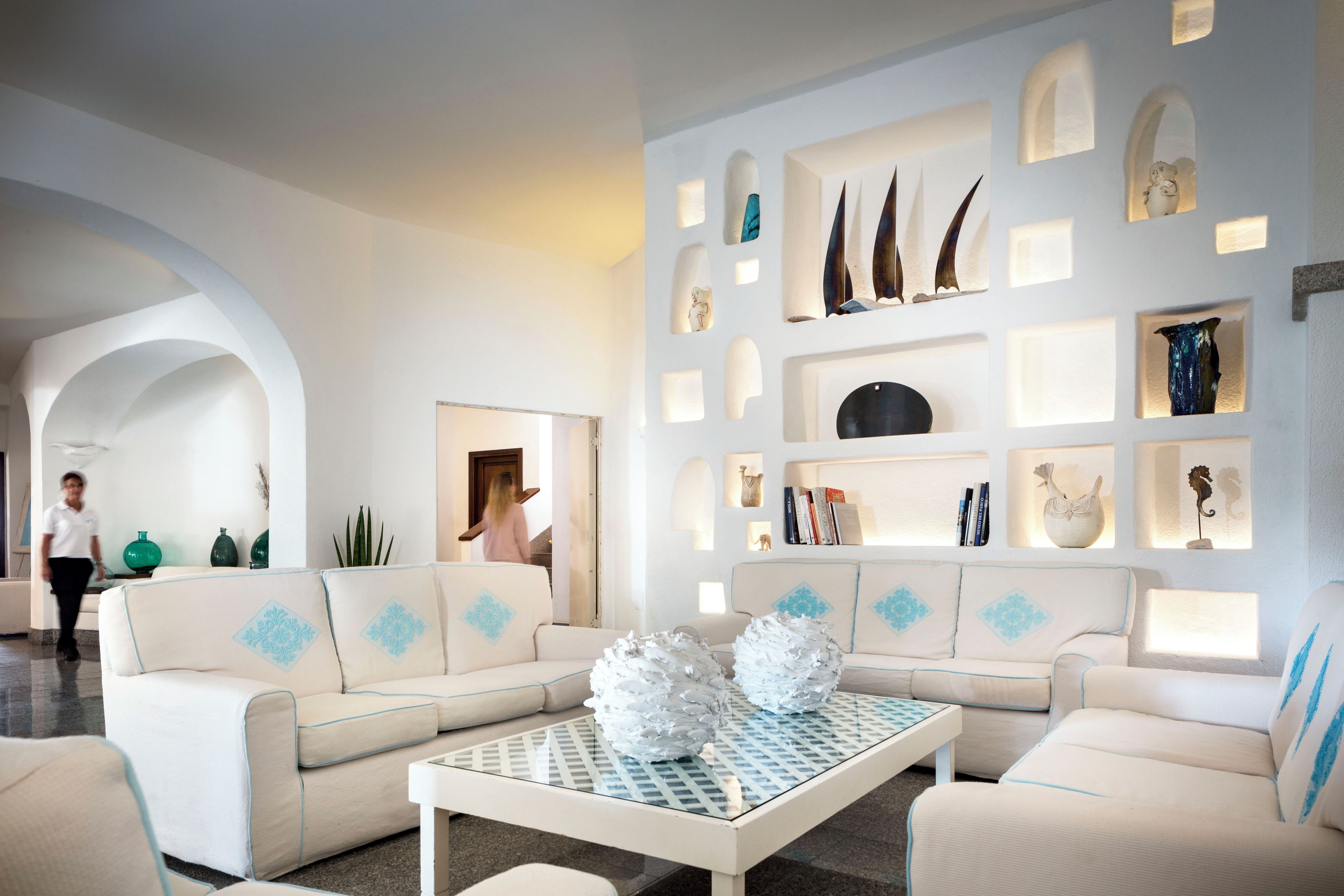 Una sala de estar moderna con un sofá modular, una mesa de centro de vidrio y objetos decorativos en estanterías.