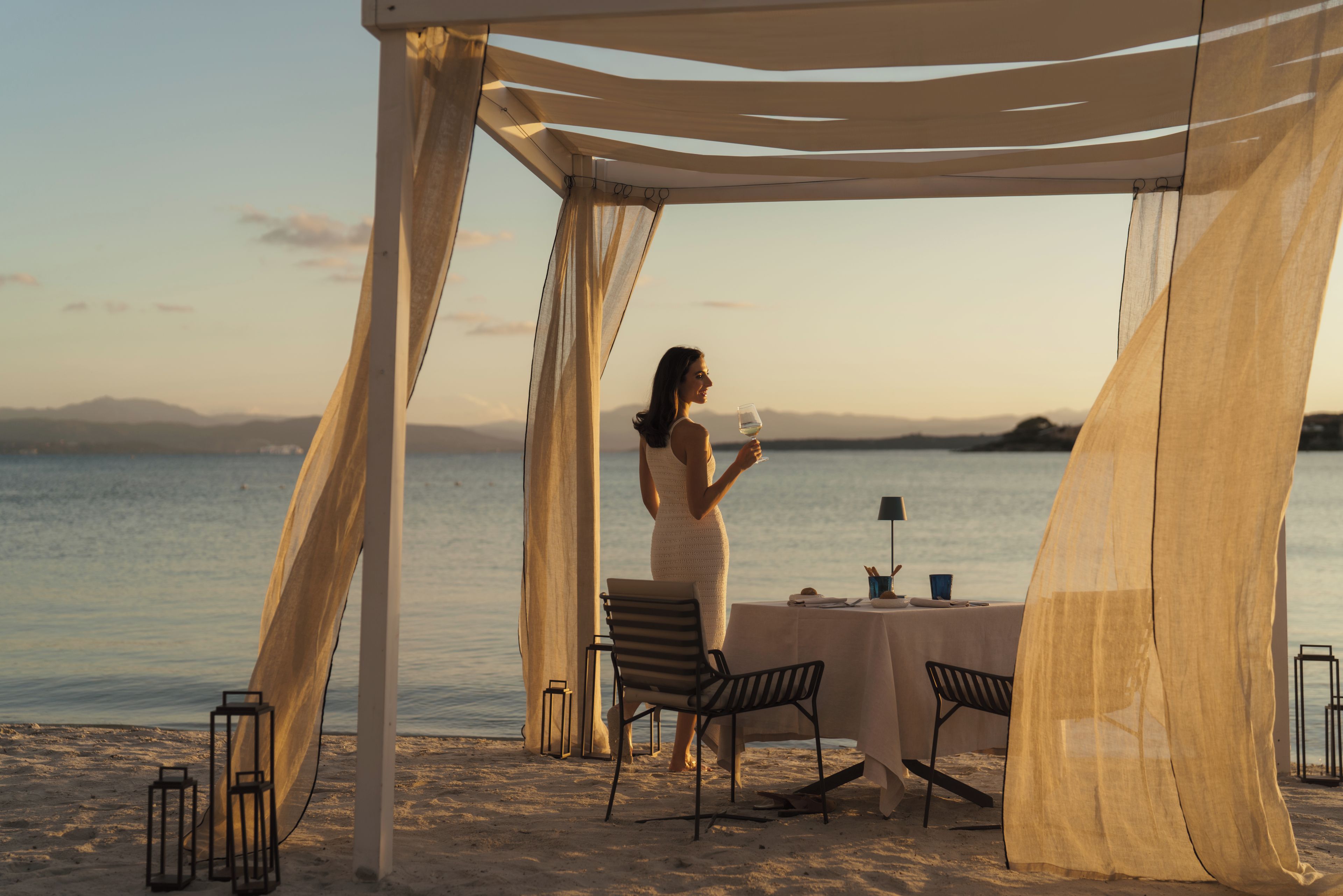 A beachside dining setup with a table and chairs under a canopy, overlooking the sea.