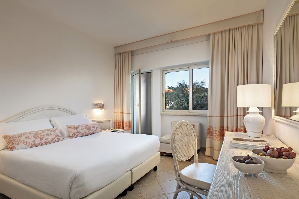 Een hotelkamer met een bed, een bureau met lamp, een stoel en een schaal fruit.