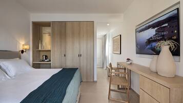Een hotelkamer met een bed, een houten garderobe, een bureau met stoel, en een groot raam met uitzicht op een wateroppervlak.