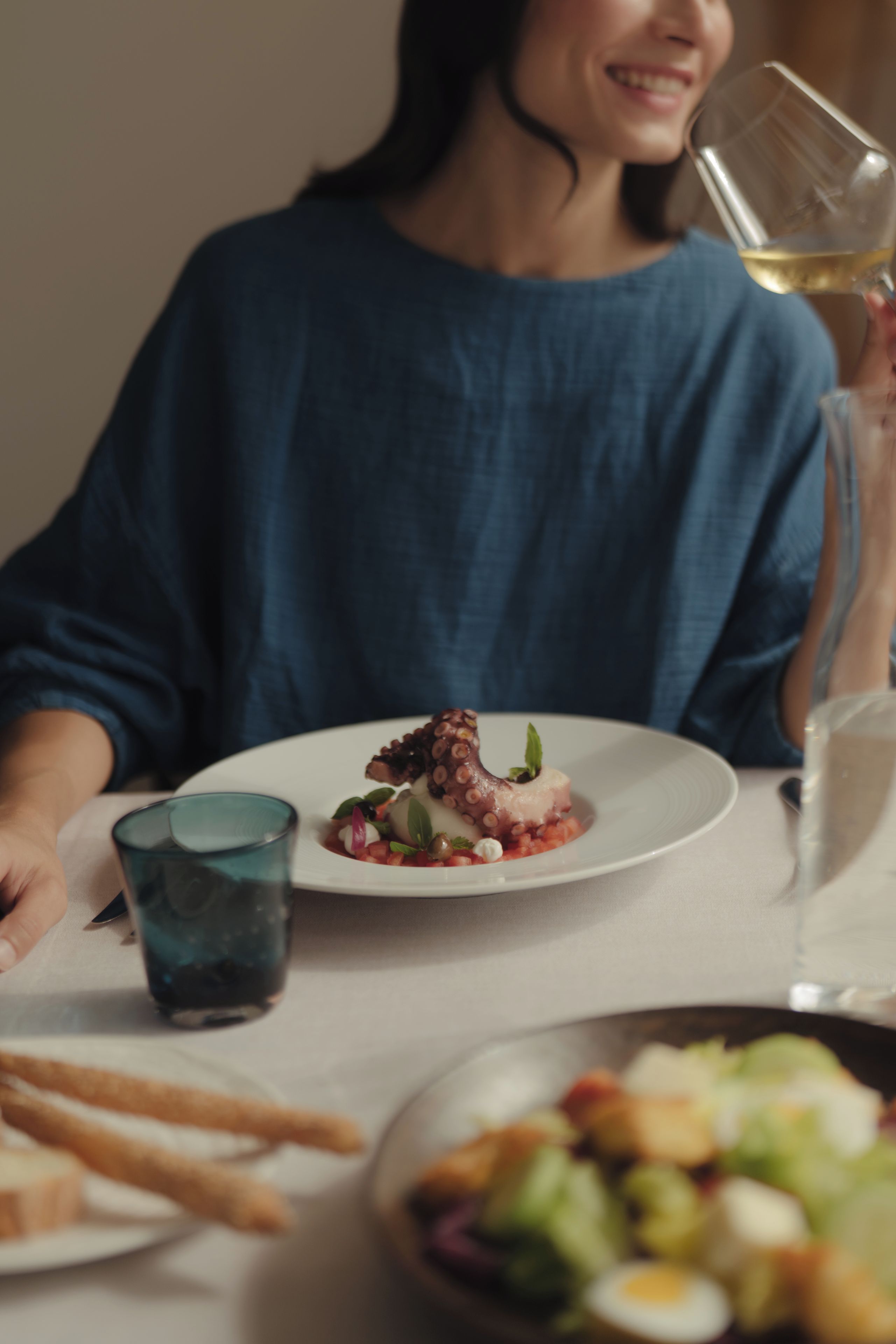 A person seated at a table with a plate of food, a glass of white wine, and a glass of water.