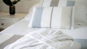 A neatly made bed with striped pillows, a white bathrobe, and a vase with orchids on a bedside table.