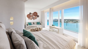 Une chambre moderne avec un grand lit, un coin salon comprenant un canapé et des fauteuils, une petite table et une vue sur la mer.
