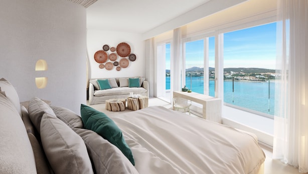 Un dormitorio moderno con una cama grande, una zona de estar con sofá y sillones, una mesita y vistas al mar.