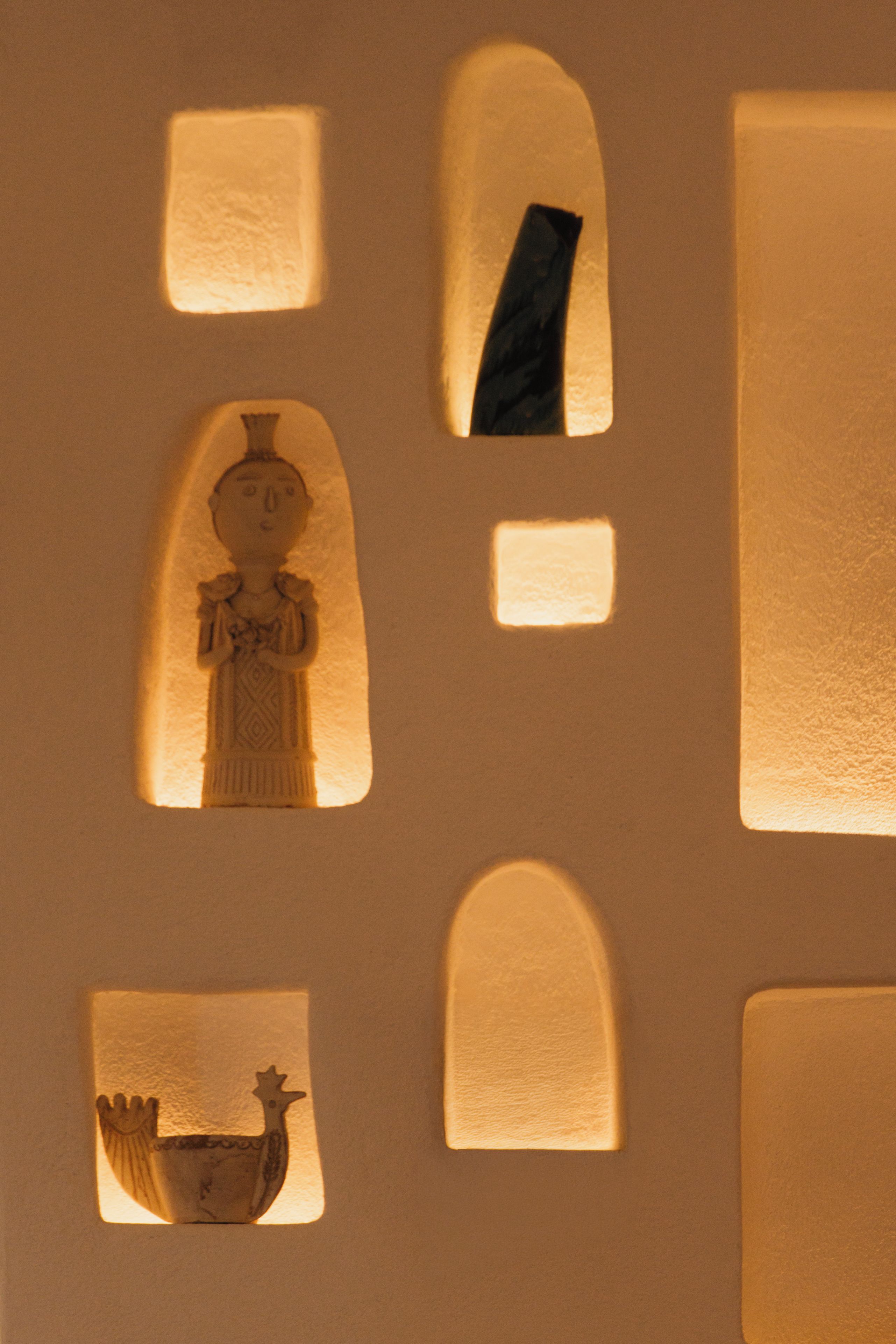A wall with multiple rectangular and arched cutouts, some containing silhouettes of objects and figures.
