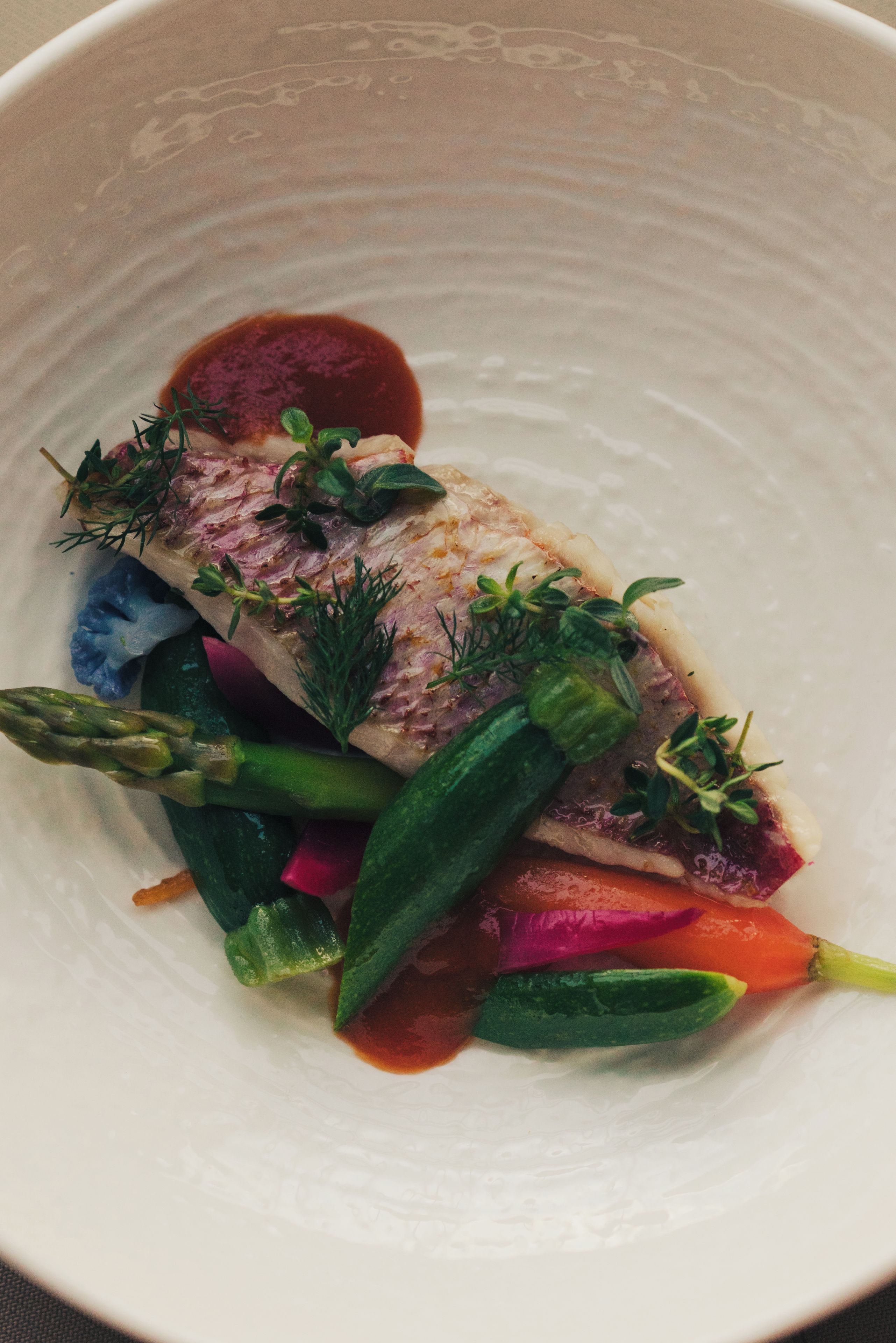 A white plate with a piece of fish, asparagus, and a red sauce.