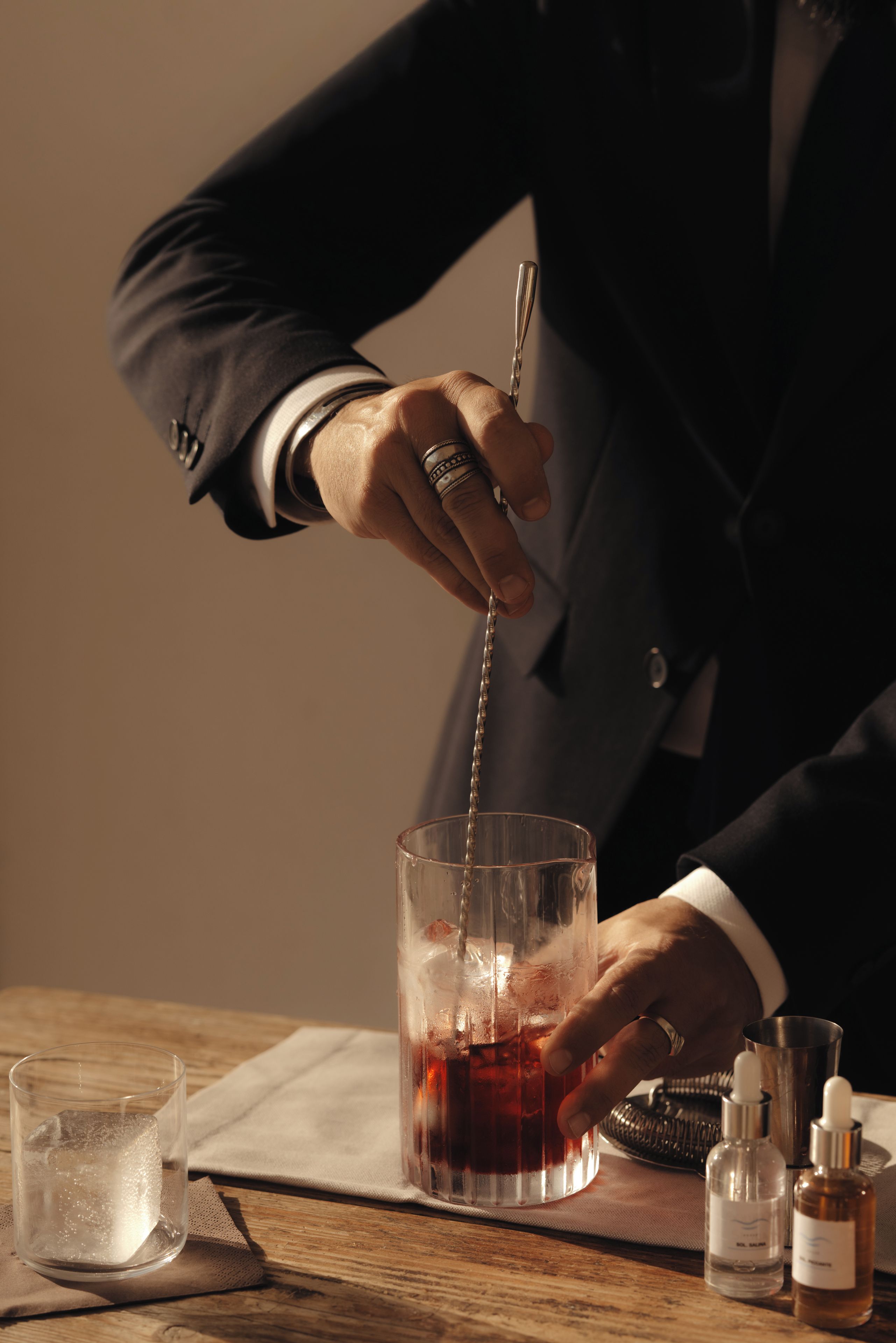 Una persona in giacca versa un drink in un bicchiere con ghiaccio.