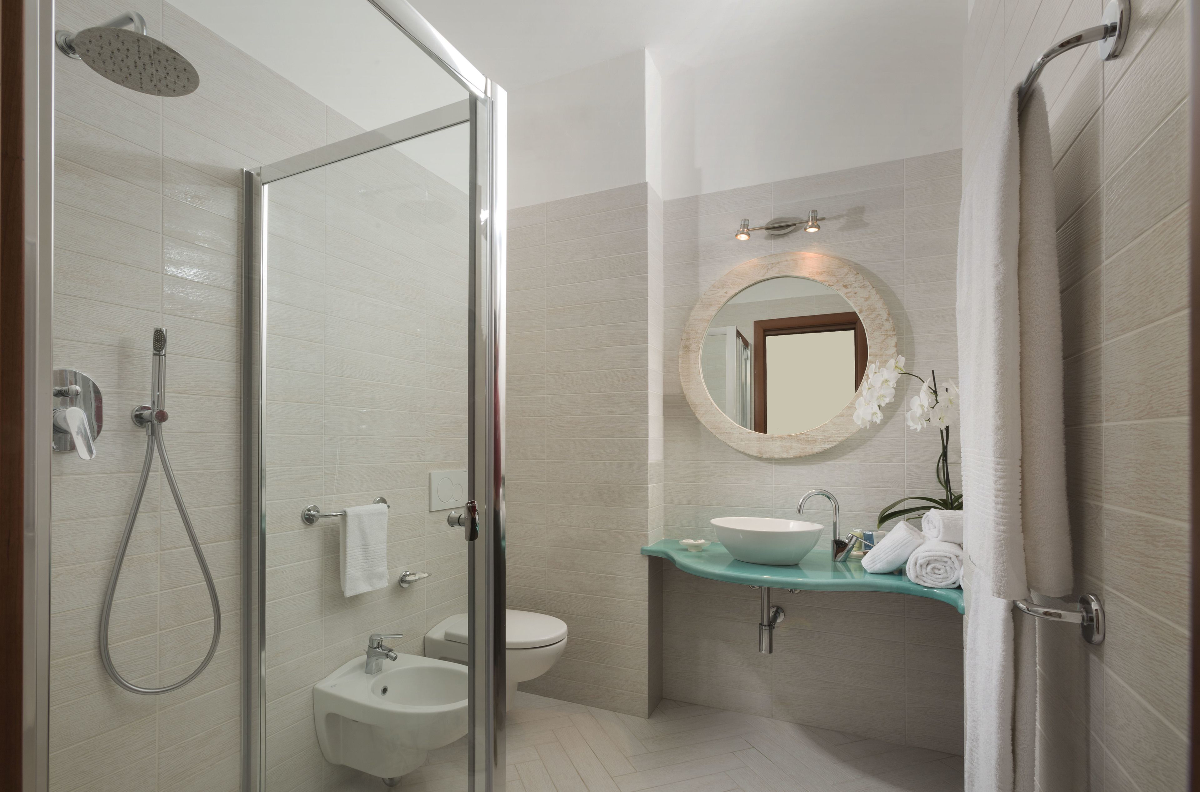 Un bagno moderno con doccia vetro, lavabo su piedistallo e mobile vanità con specchio.