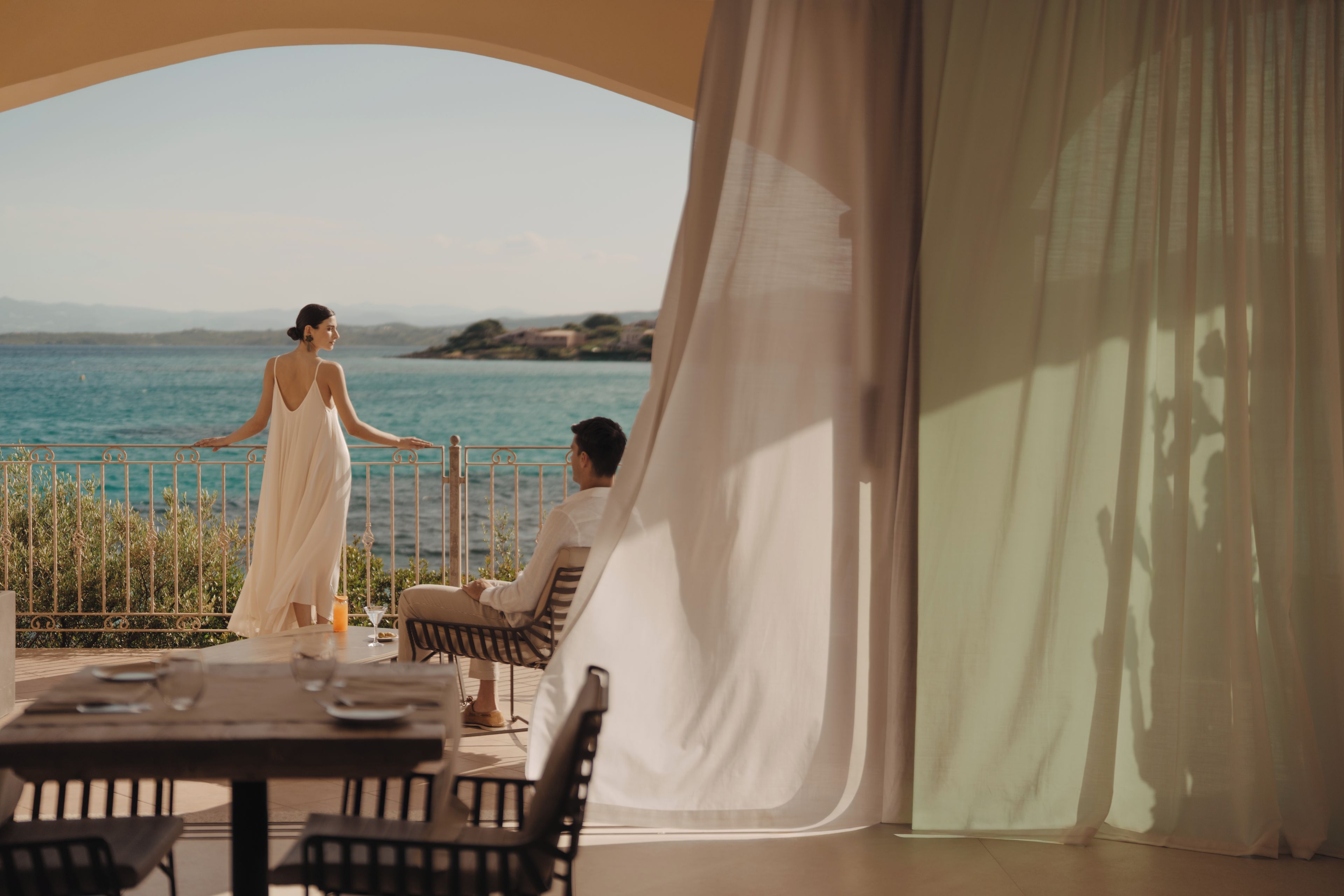 A couple seated at a table with a view of the sea and hills in the background.