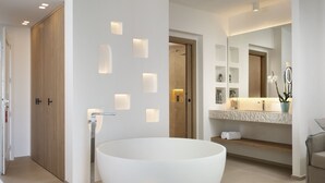 Een moderne badkamer met een vrijstaand ligbad, inbouwspots en een wastafel met spiegel en planken.