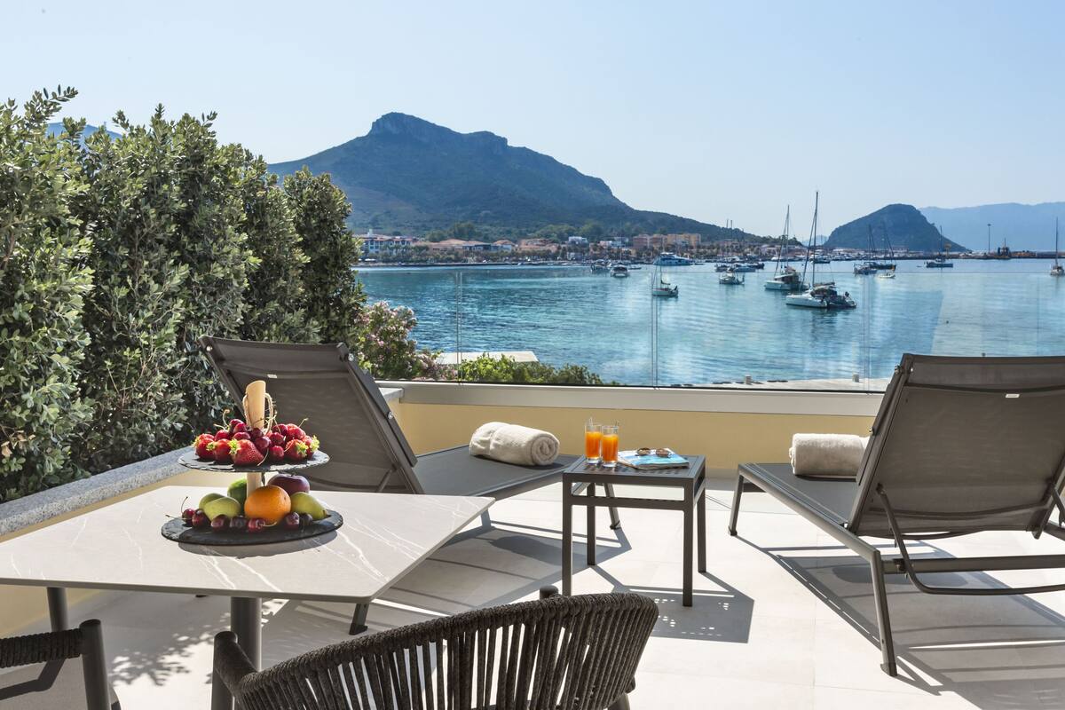 Eine Terrasse mit Frühstückstisch, mit Blick auf einen Yachthafen, Boote und einen Berg im Hintergrund.