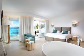 Een moderne hotelkamer met een groot bed, een zithoek met een stoel en bijzettafels, een badkuip en een balkon met uitzicht op zee.
