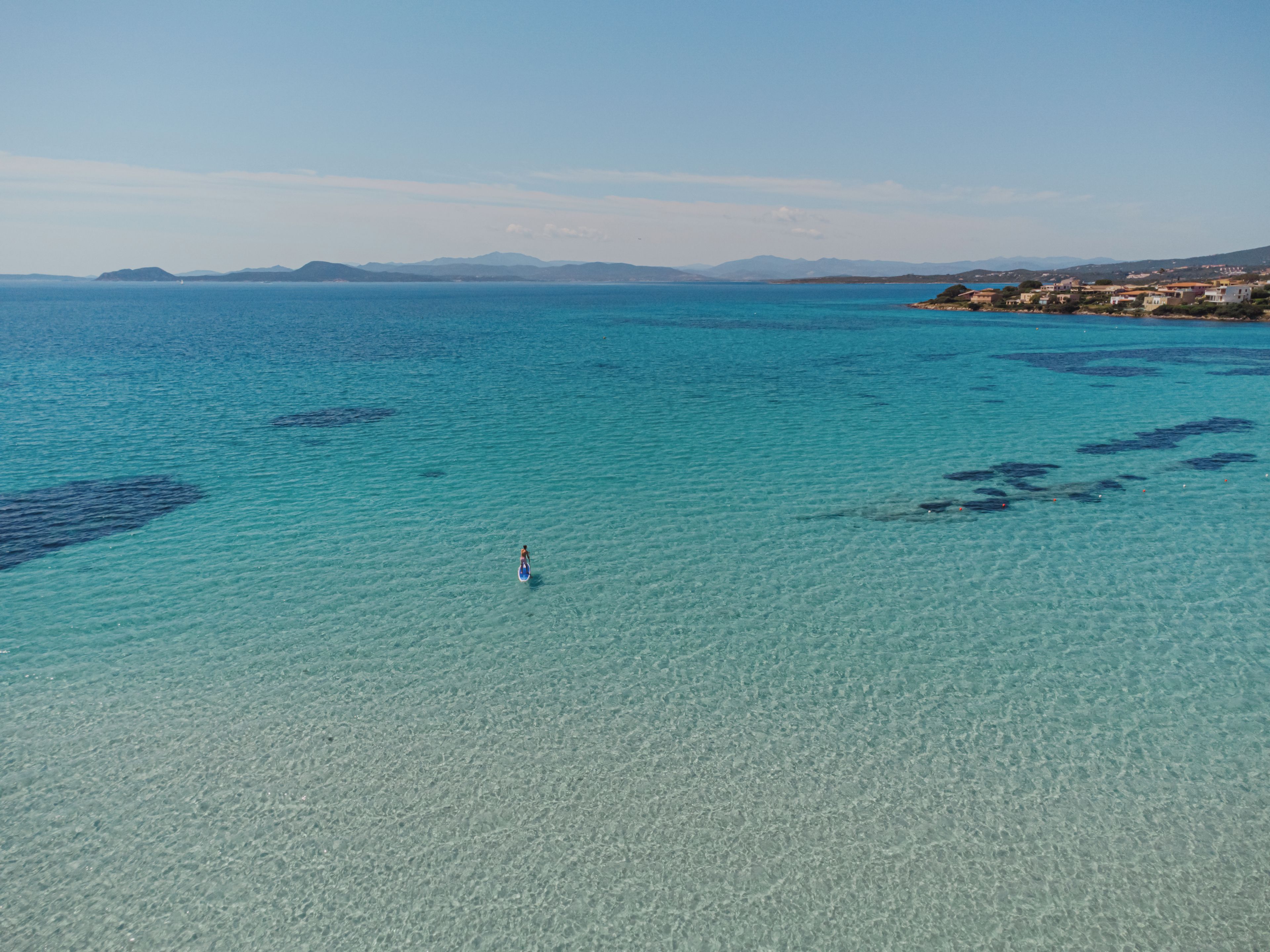 Een kustlandschap met helder turquoise water en verre bergen.
