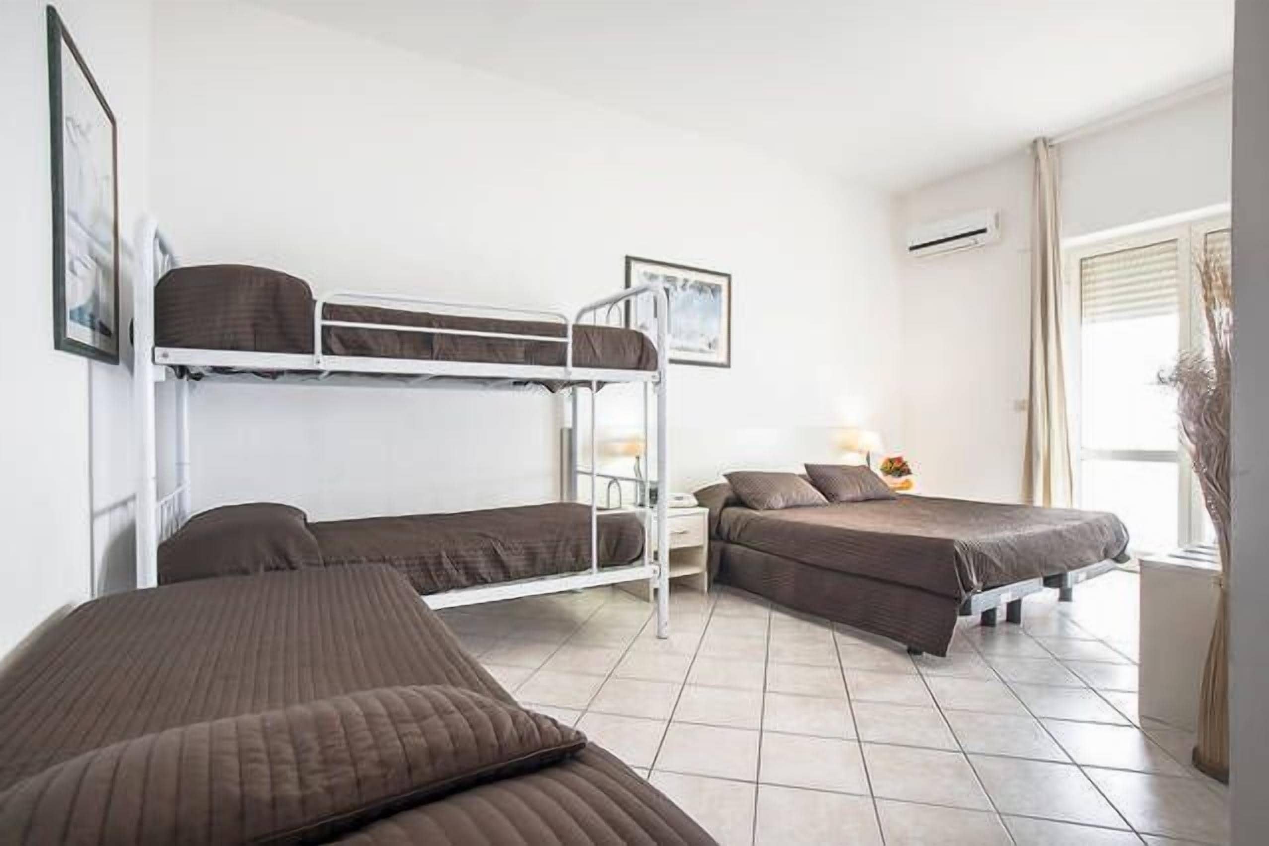 A room with bunk beds, a bedside table with a lamp, and a window with curtains.
