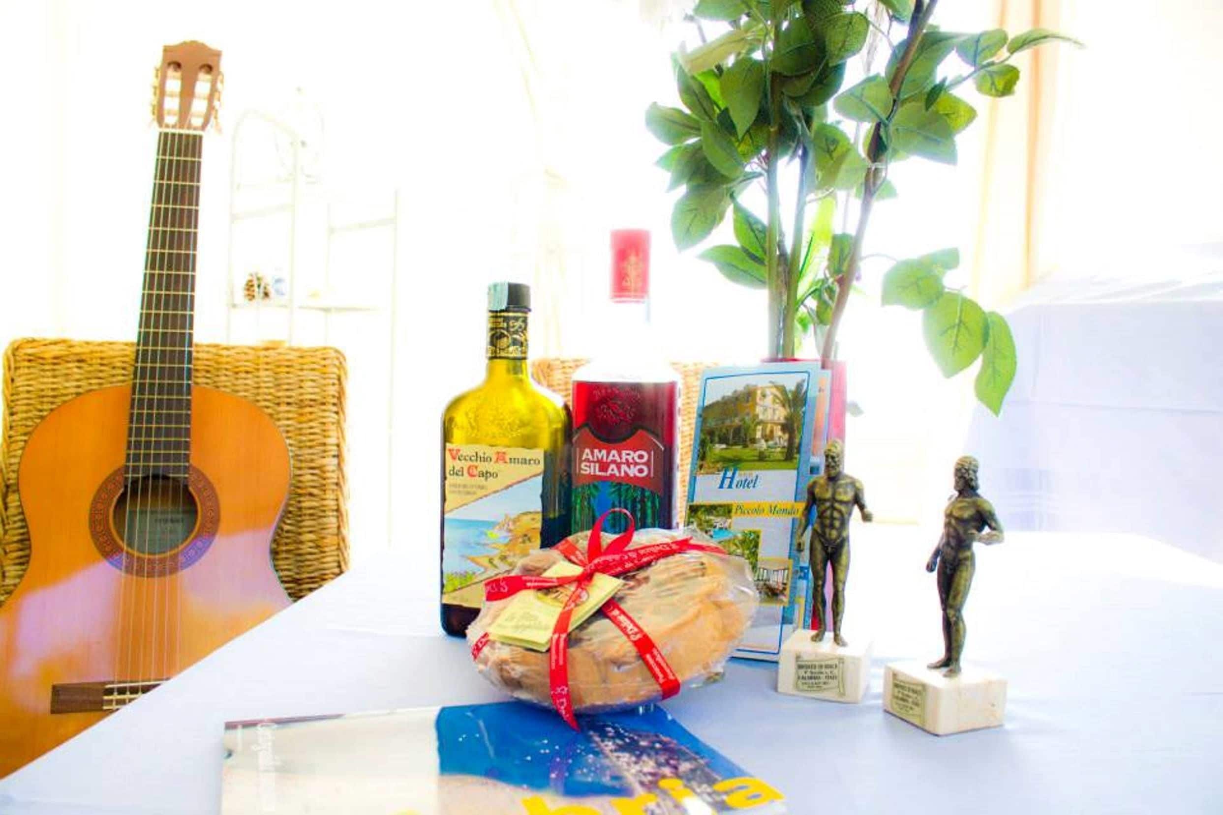 Una mesa con una guitarra, una botella de vino, un regalo envuelto, un libro y una planta.