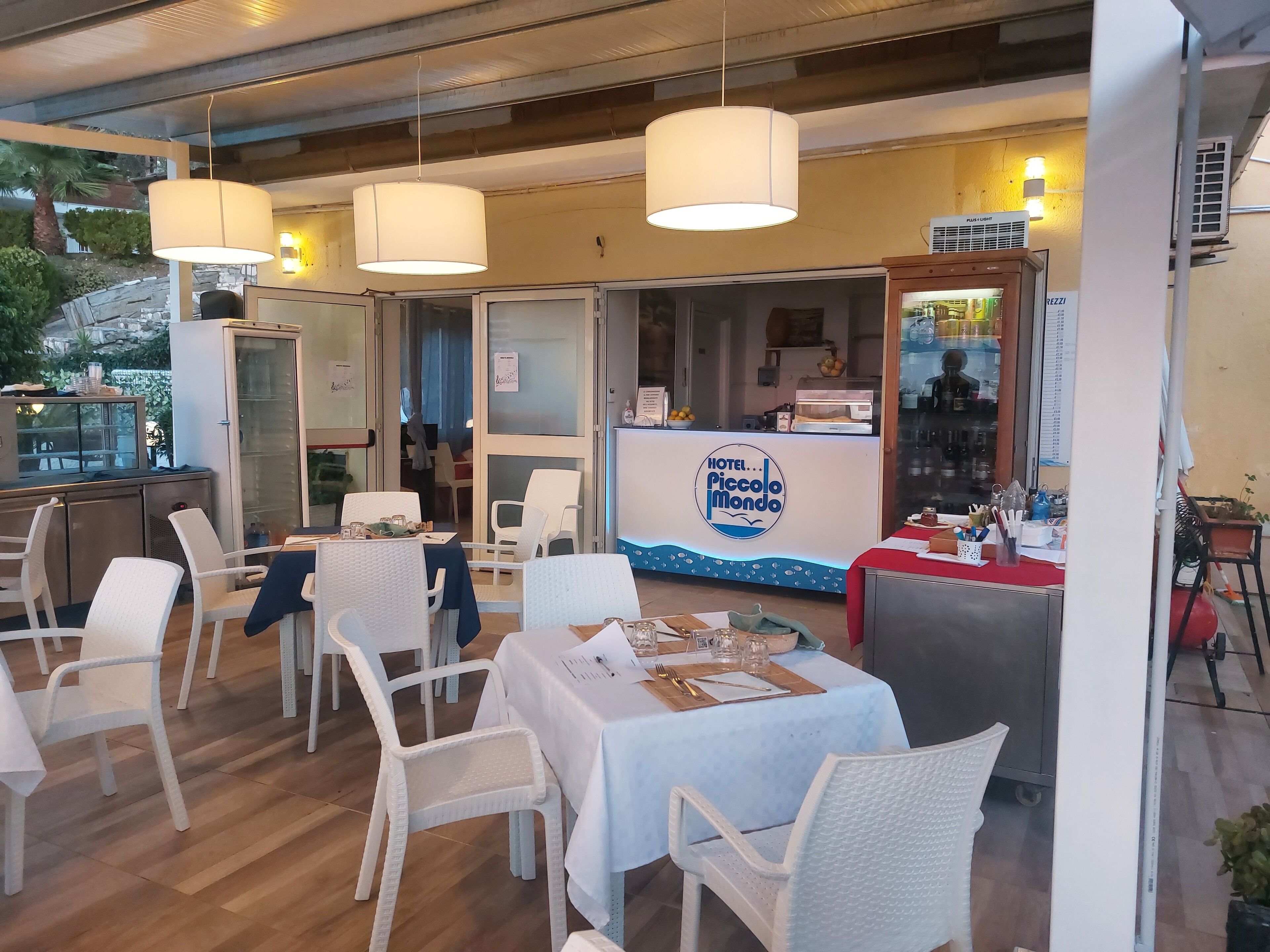 A restaurant with white chairs and tables, a counter with a menu, and hanging lights.