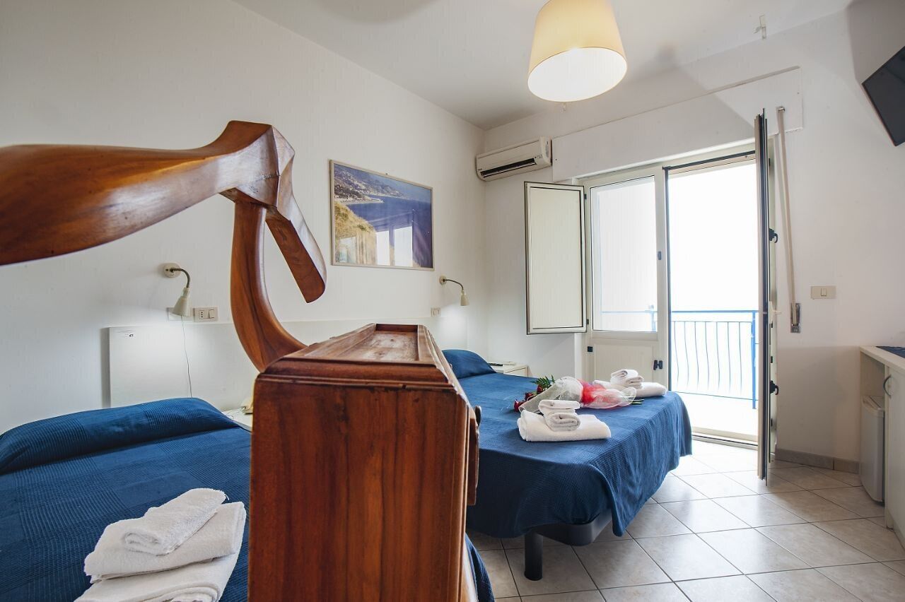 Habitación de hotel con dos camas, cabecero de madera, balcón con vistas y un cuadro en la pared.