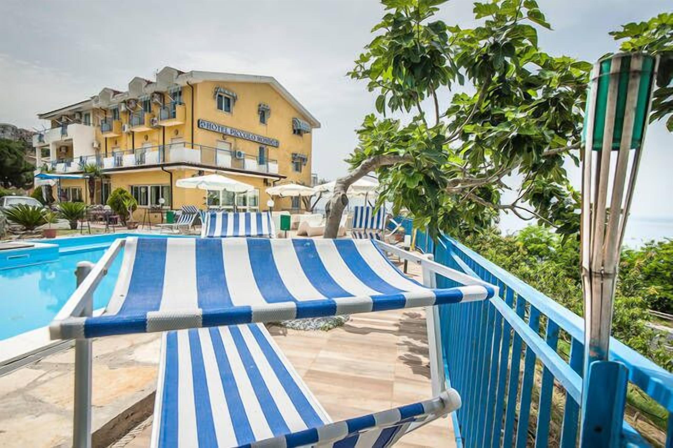 A hotel with a pool area, striped lounge chairs, and a building with balconies.