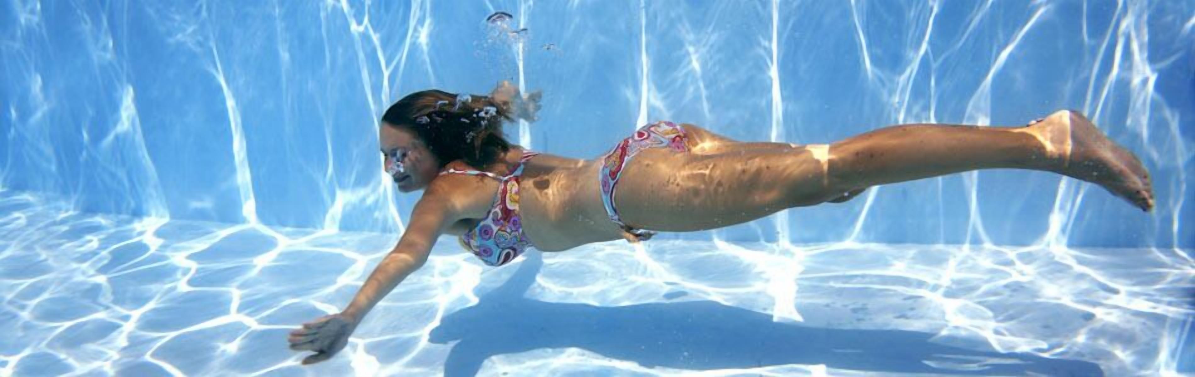 A person swimming in a clear blue pool with a tiled floor.