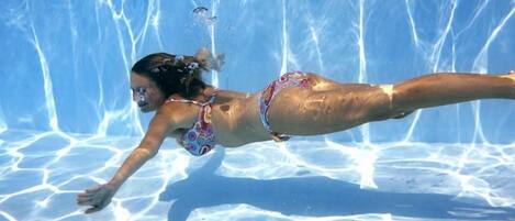A person swimming in a clear blue pool with a tiled floor.