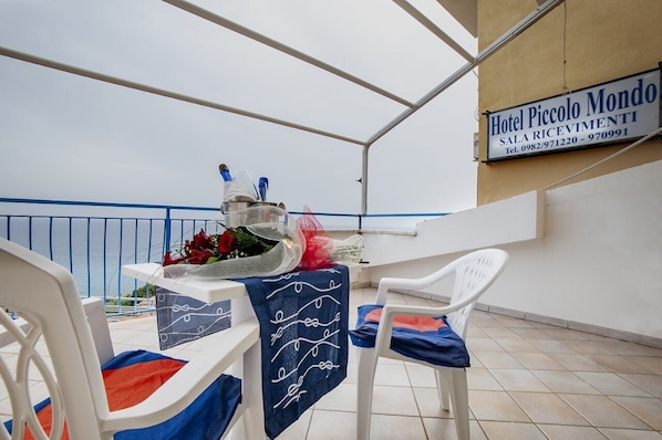 A balcony with a table set for two, chairs, and a sign for Hotel Piccolo Mondo.