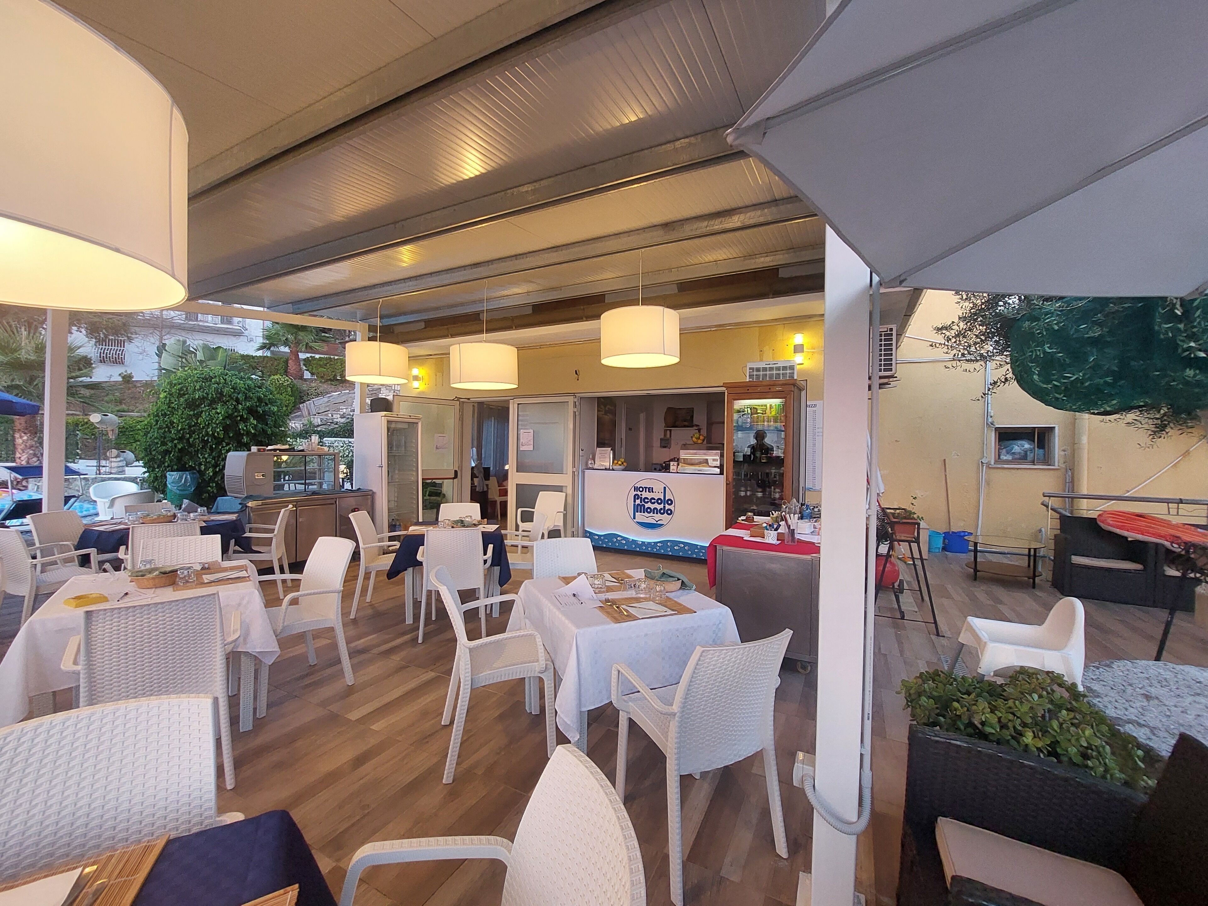 Un área de comedor al aire libre con sillas y mesas de mimbre blanco, una barra con un letrero que dice 