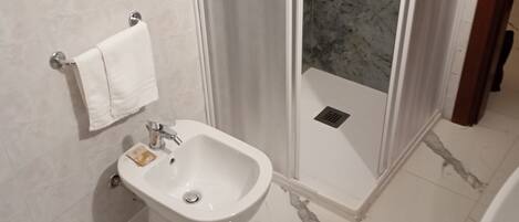 A bathroom with a bidet, a toilet, and a shower area with a glass door.