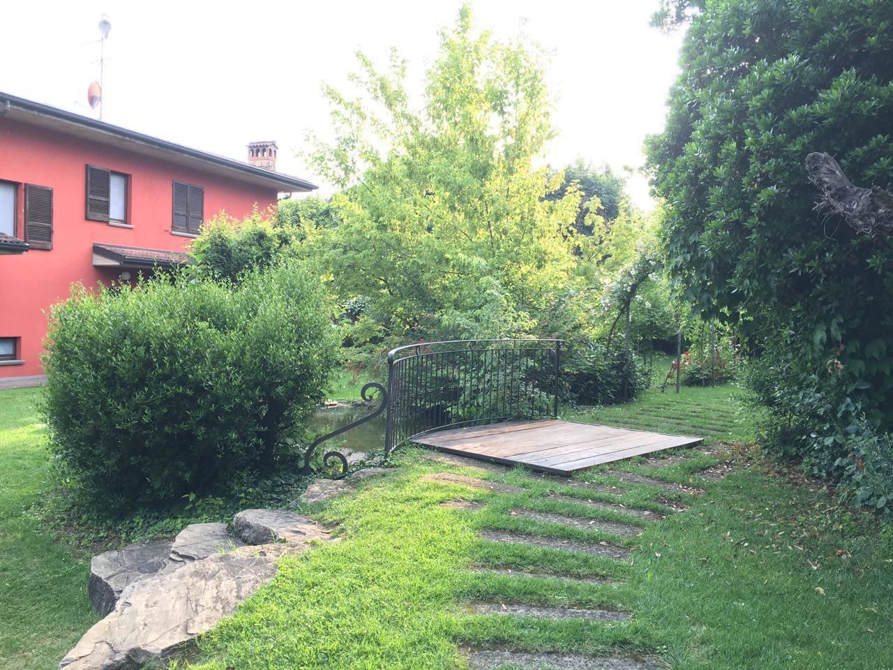 Un giardino con una terrazza in legno, gradini in pietra e una recinzione in metallo.