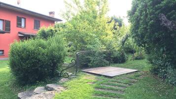 Un giardino con una terrazza in legno, gradini in pietra e una recinzione in metallo.