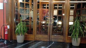A hotel entrance with wooden double doors, potted plants, a fire extinguisher, and a green exit sign. - Il Leone D'Oro (Telgate)