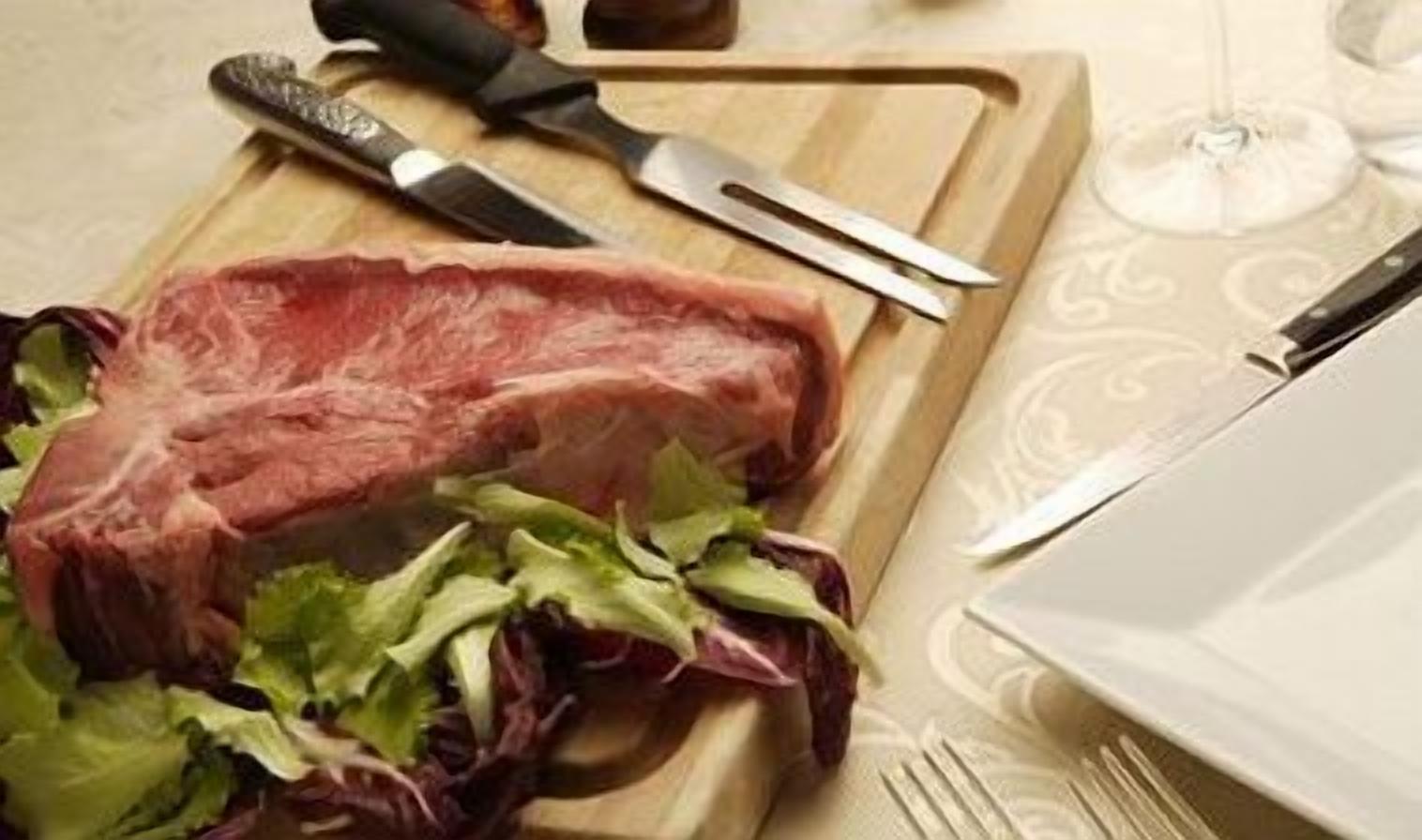 Un bistec sobre una tabla de madera con un cuchillo y un tenedor a un lado.