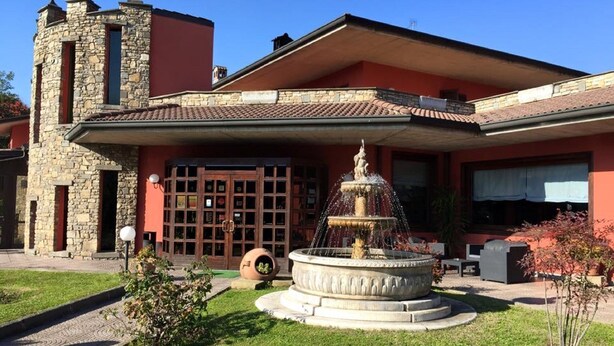 A building with a stone facade, a large window with a grid pattern, and a fountain in the front yard. - Il Leone D'Oro (Telgate)