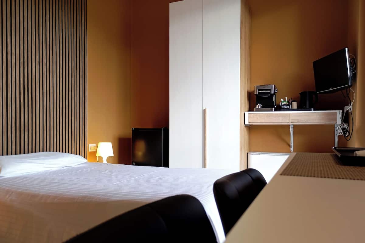 A hotel room with a bed, a desk with a computer, a TV, and a coffee maker.