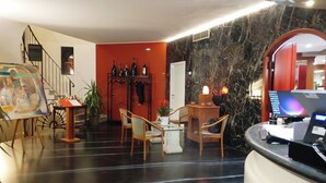 A hotel lobby with a marble floor, a reception desk, a seating area with chairs, a coat rack, and a painting on easel. - Il Leone D'Oro (Telgate)
