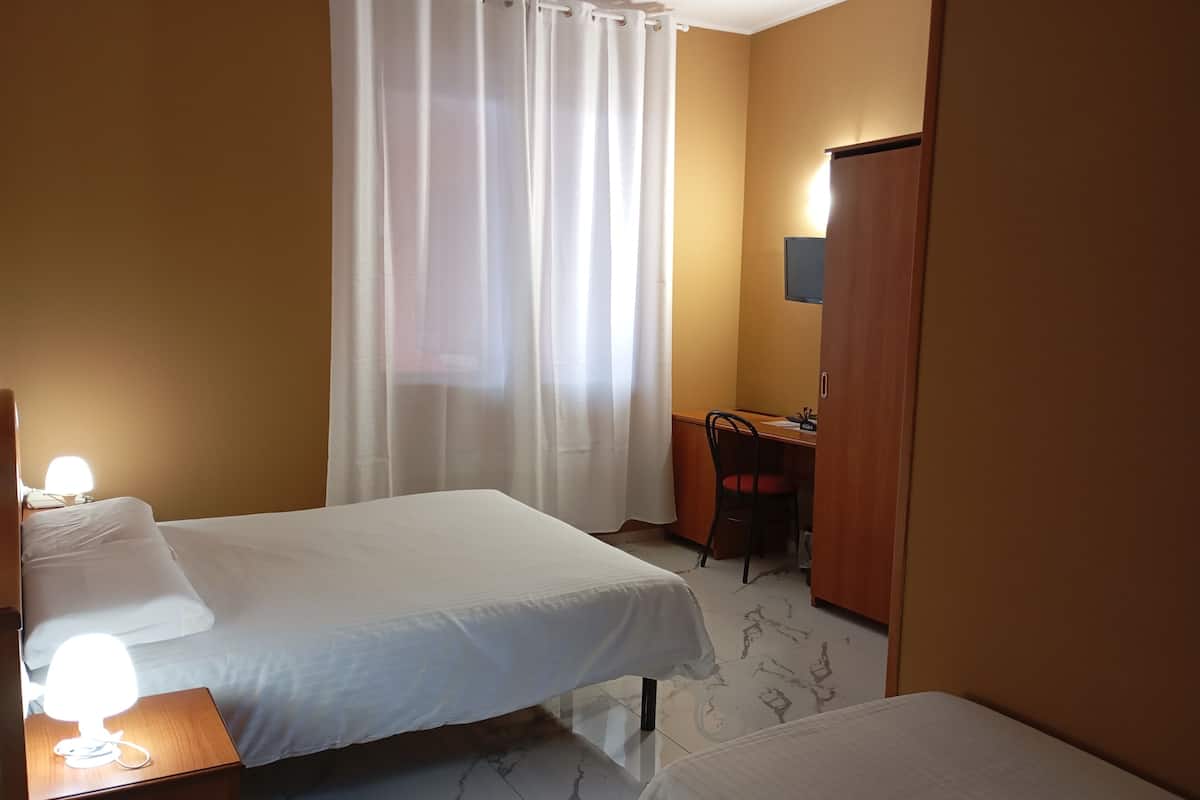 A hotel room with two beds, a desk, a chair, a wardrobe, and a curtain.