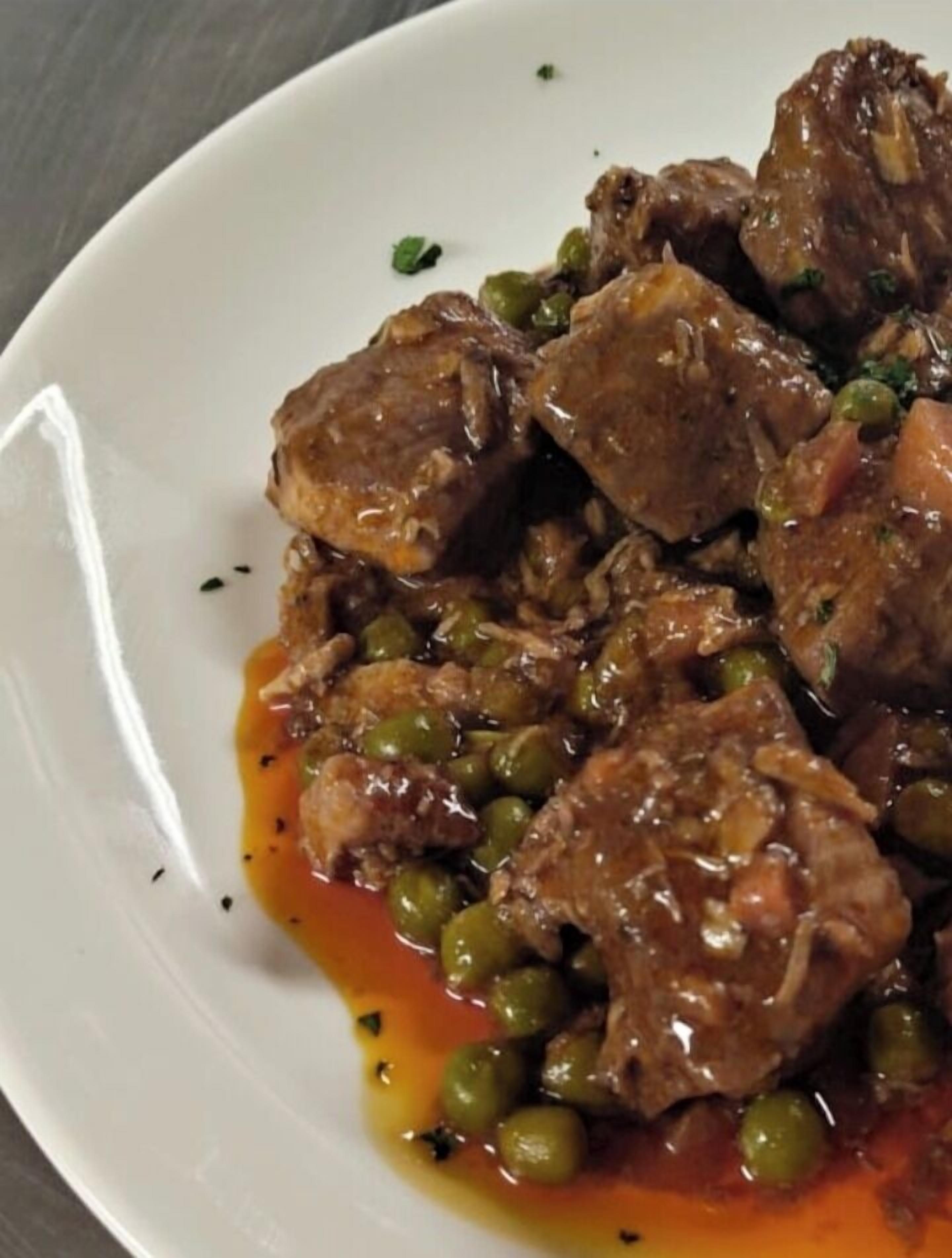 A white plate with a dish of meat and green peas in a brown sauce.