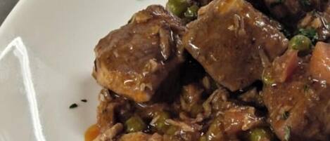 A white plate with a dish of meat and green peas in a brown sauce.