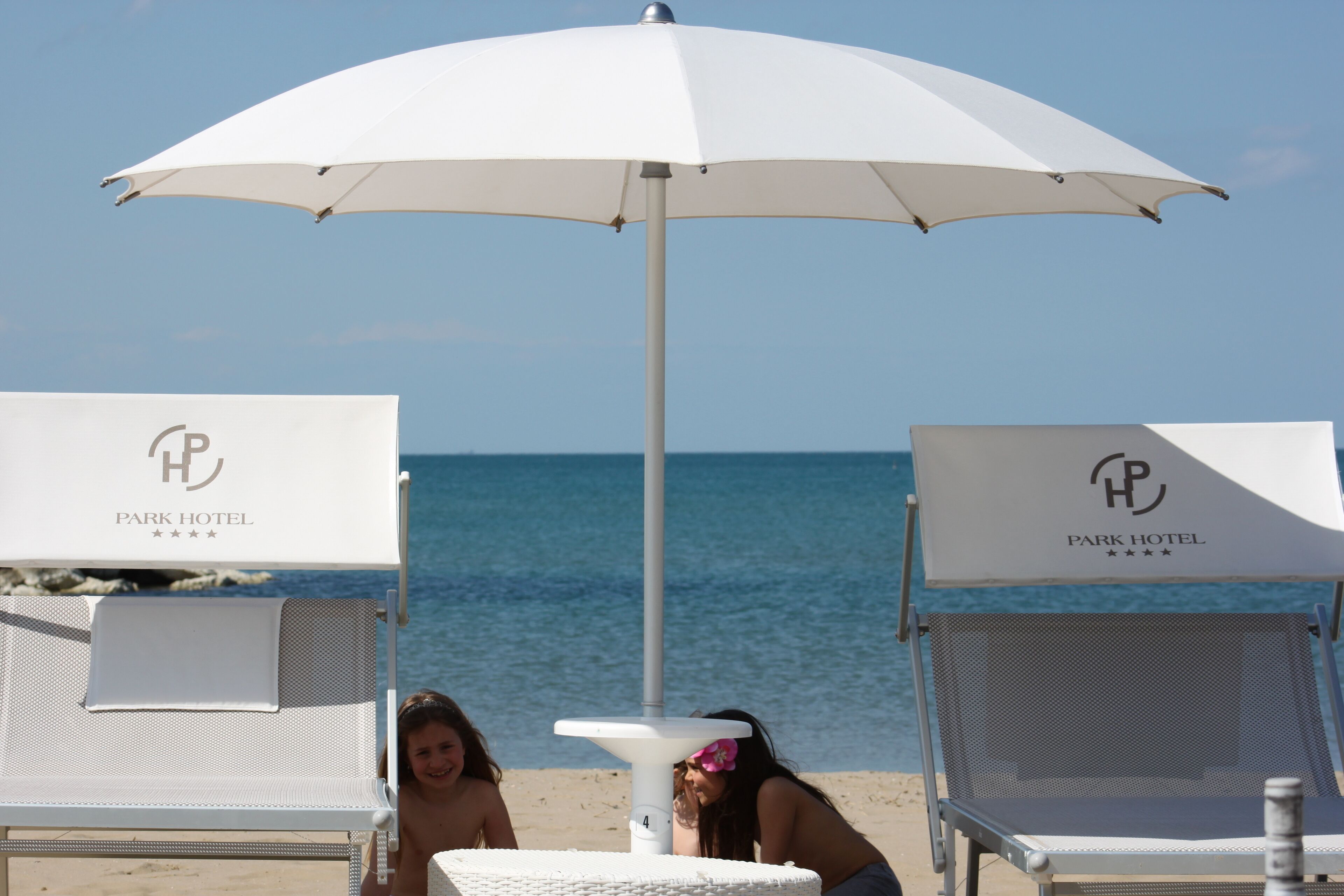 Two white lounge chairs with 'Park Hotel' branding, a white umbrella, and a small table with a white cloth.