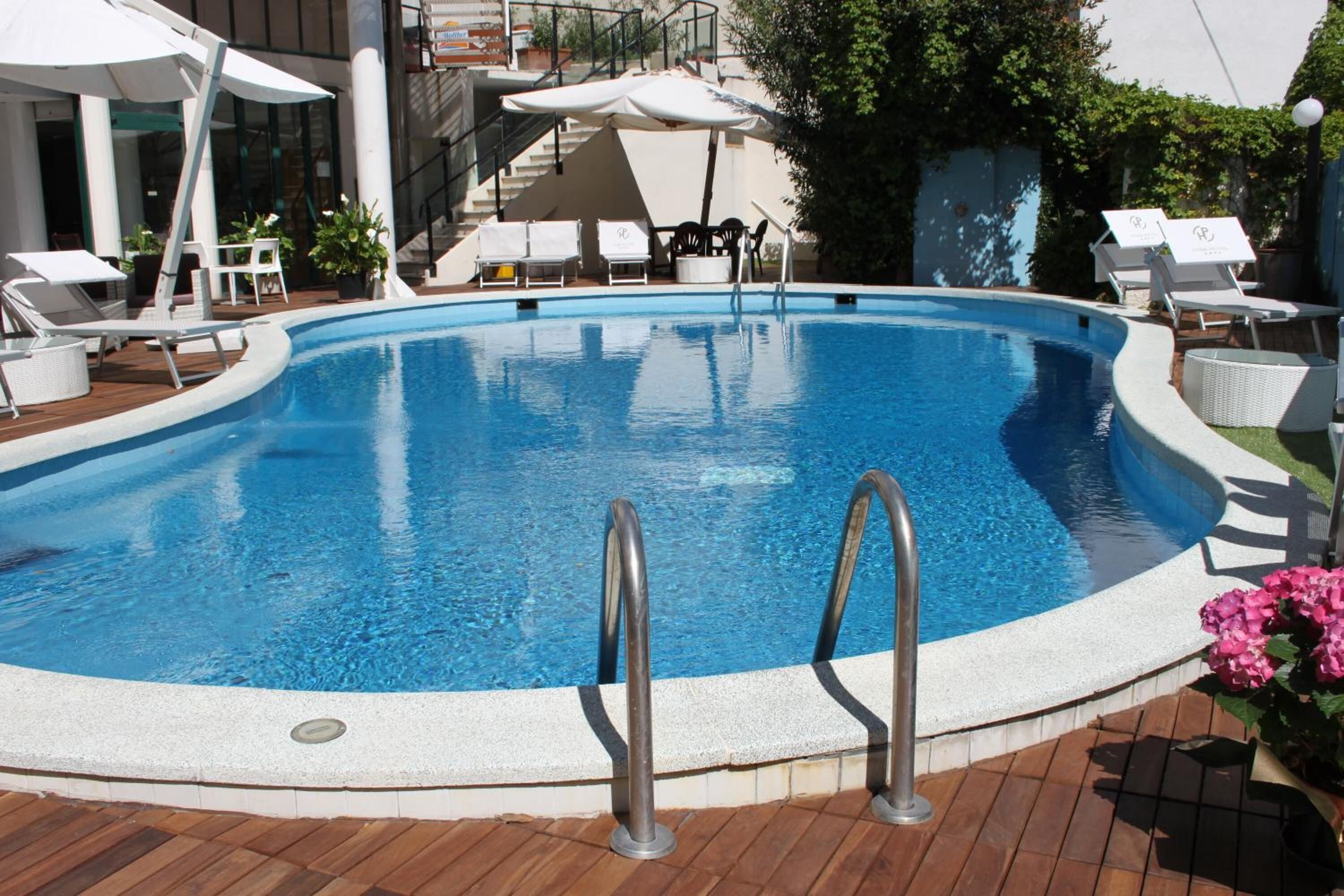 A swimming pool with lounge chairs and umbrellas, surrounded by a wooden deck and potted plants.