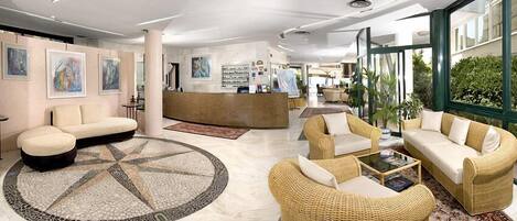 Un vestíbulo amplio con mostrador de recepción, zonas de estar cómodas y grandes ventanales con vistas al exterior.