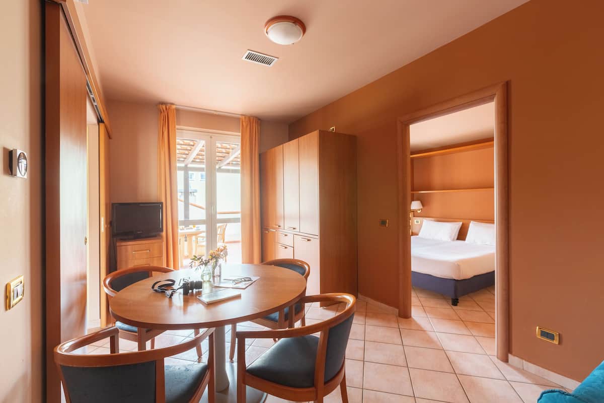 A hotel room with a bed, a TV, a dining table with chairs, and a kitchenette.