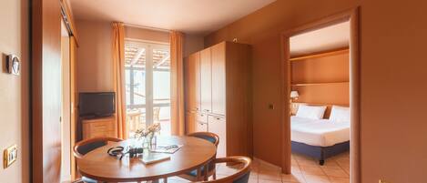 A hotel room with a bed, a TV, a dining table with chairs, and a kitchenette.
