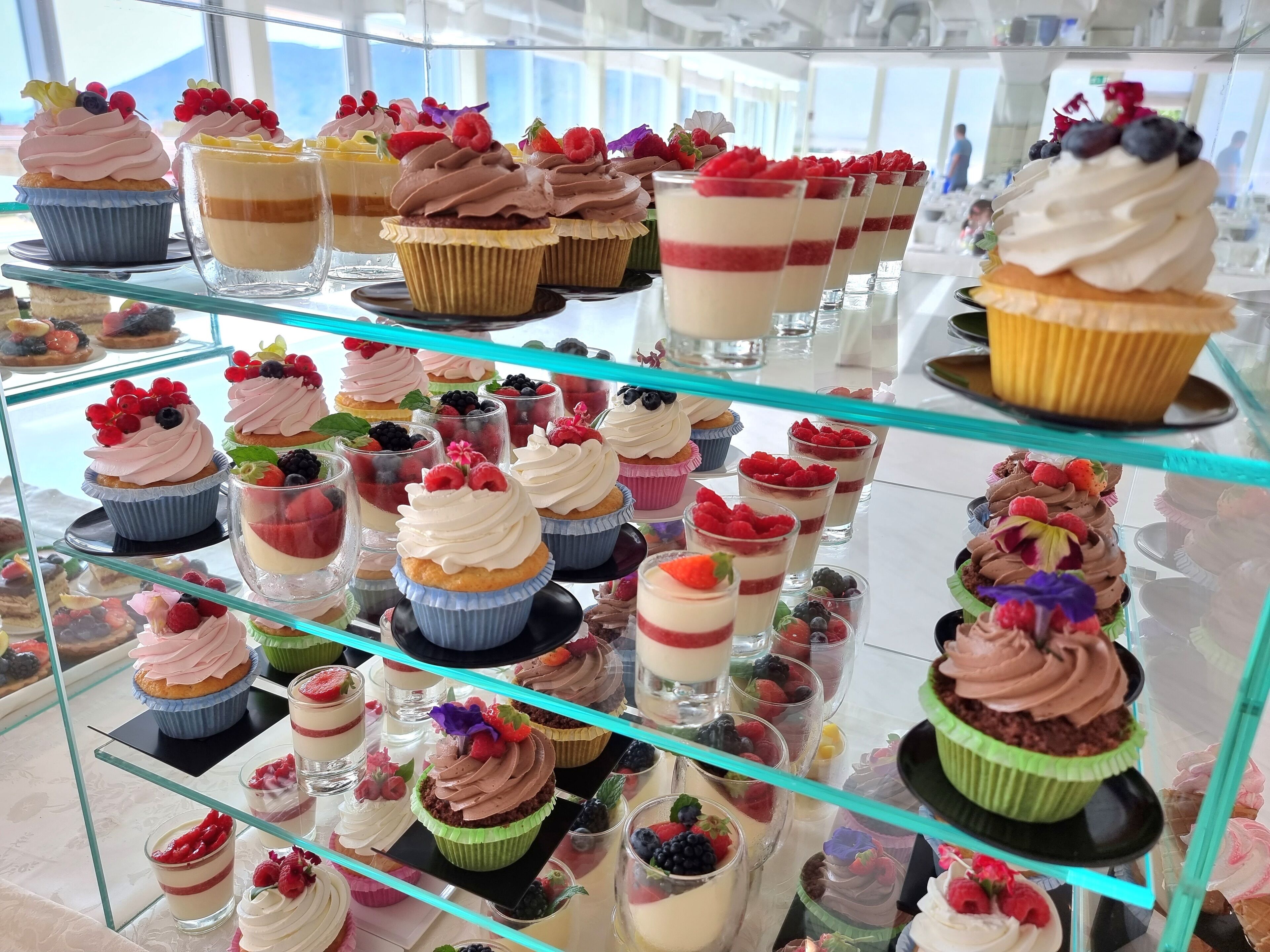 Una variedad de postres exhibidos en estantes de vidrio en un espacio bien iluminado con luz natural.