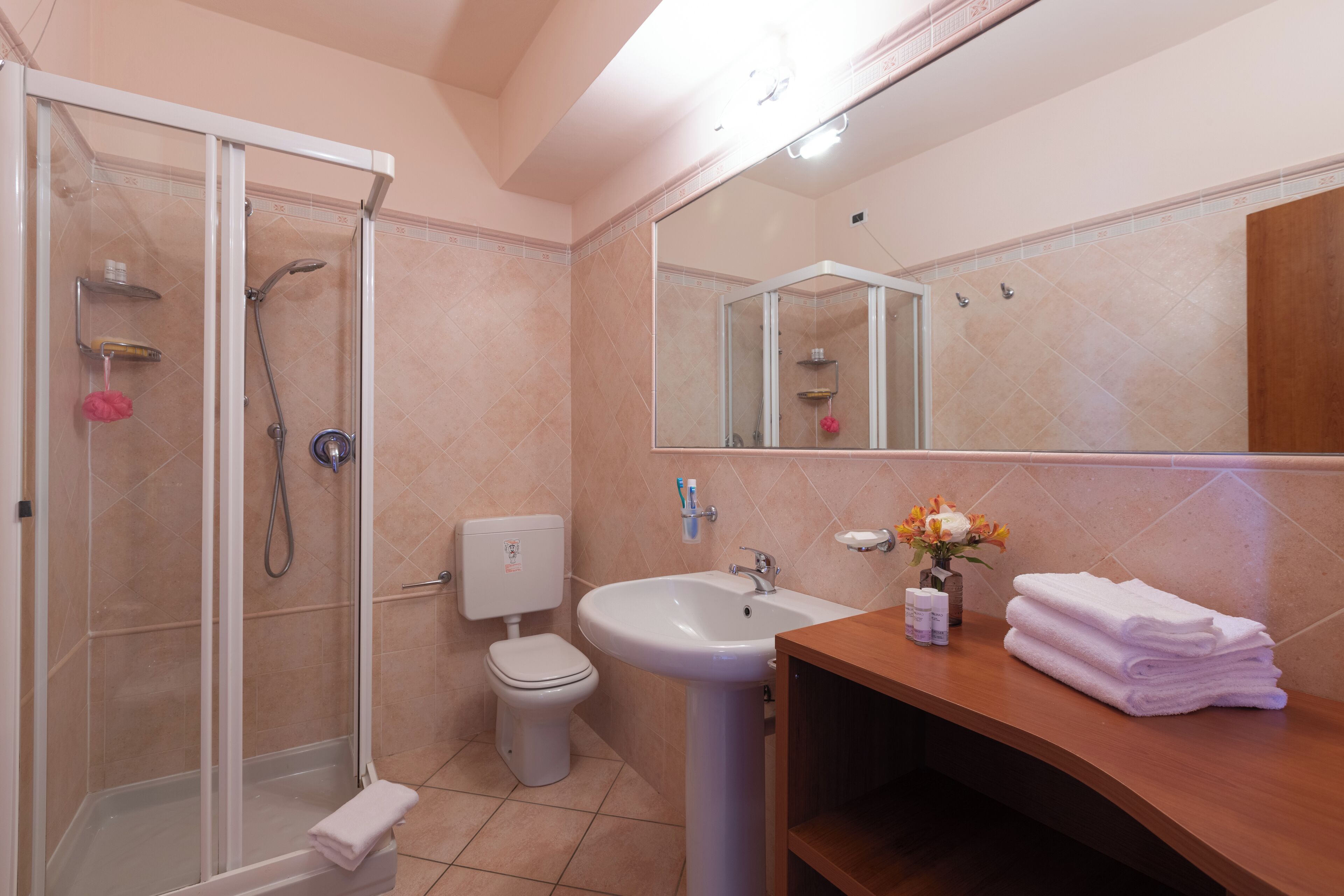 Un baño con ducha de vidrio, inodoro, lavamanos y tocador con toallas.
